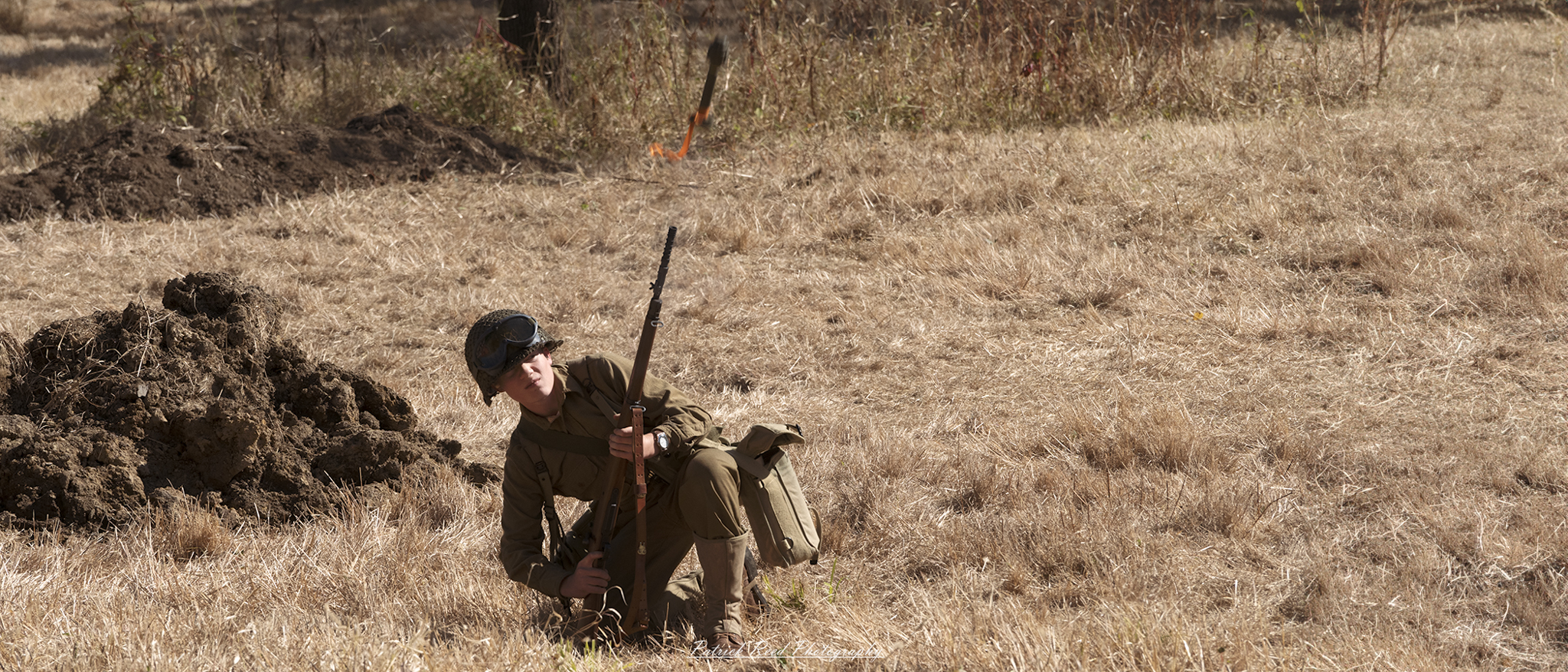 "Image of a soldier firing a rifle grenade from an M1 Garand during World War II. The soldier is positioned in a combat-ready stance, with the rifle held at shoulder level, as the grenade is launched from the barrel. The scene captures the intensity of battle, with dirt and debris flying around him. The soldier's uniform is typical of the era, featuring a helmet and gear appropriate for the time. The background depicts a war-torn landscape, emphasizing the action and urgency of the moment."